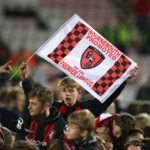 Bournemouth fans celebrating in the stands with a club's flag.